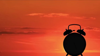 Time lapse of silhouette of alarm clock ringing in the morning with sunrise background.