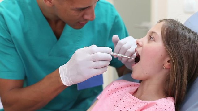 Close up of cute little girl keeping her mouth open while dental assistant examining her teeth