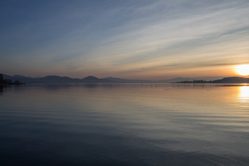 A perfectly symmetric sunset at the lake, with long and obliques clouds, distant hills and sun