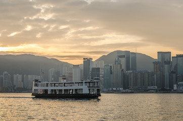 Star ferry in Victoria Harbor and HK skyline at sunrise. View from Kowloon on Hong Kong Island .