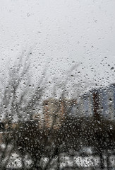 Drops of rain on window in front of city buildings