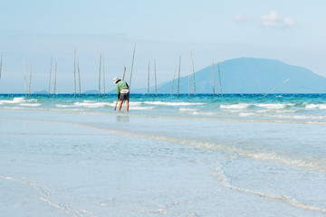 Man searching small shell from the beach. A fisherman walking on the coast and using a special equipment to collect seashells that hide in the sand
