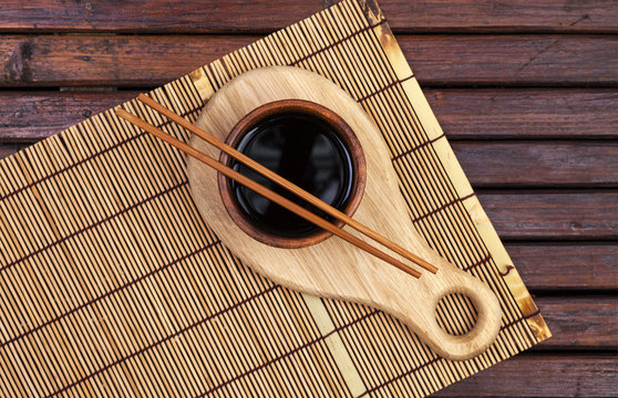 Bamboo mat, soy sauce, chopsticks on dark wooden table. Top view with copy space