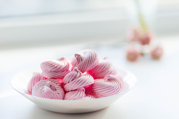 Pink marshmallows zephyr in a white plate on a brown red chair on white background copyspace