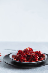 chunks of ripe red pomegranate in a white bowl on a light grey background rough table close-up copyspace