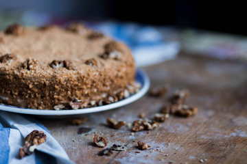 round delicious honey cake in blue white plate on a brown wooden background, bright flour, walnuts, white blue stripe kitchen towel