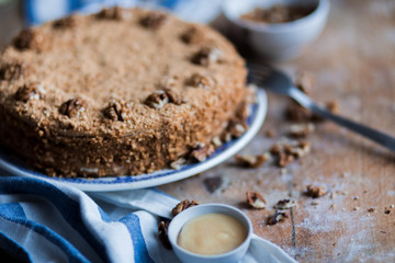 round delicious honey cake in blue white plate on a brown wooden background, bright flour, walnuts with white blue striped tea towel Golden amber honey with a fork