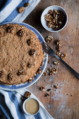 round delicious honey cake in blue white plate on a brown wooden background, bright flour, walnuts with white blue striped tea towel Golden amber honey with a fork