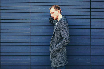 Young stylish handsome man in coat posing next to a blue wall. copy space