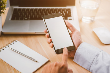 Businessman hand holding a phone with isolated screen over the desk in the office