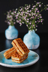 food photo three delicious wafers with white filling in the pale blue bowl vases with baby's breath on black dark background close-up