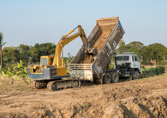 Yellow backhoe digging soil fill in rear truck