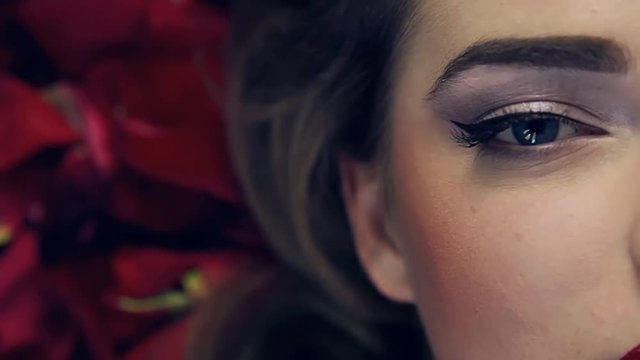 Video footage shot closeup of girl's eye with beautiful makeup.Girl opens and closes her eye.Slow motion.Professional lighting on face girl in studio.In frame half face,beautiful hairstyle,rose petals