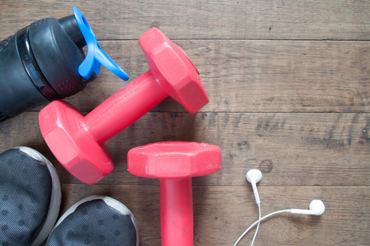 Flat lay of fitness and workout accessories, red dumbbells, water bottle and sneakers on wood background