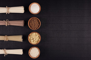 Bundles raw noodles with ingredient in wooden bowls on black striped mat background with copy...