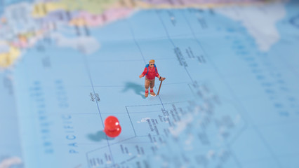 Traveler miniature mini figure with backpack walk on world map with red pin. Travelling concept.