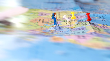 Traveler miniature mini figure with backpack walk on world map with pin and airplane. Travelling concept.