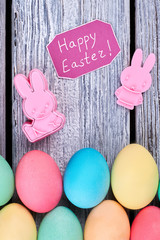 Bright Easter eggs, gray wood. Plastic rabbits and greeting card. Cheap Easter merchandise.