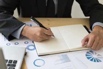 Businessman analyzing charts and graphs and taking notes.