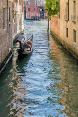 Fototapeta na wymiar Gondolier leans one leg on a wall of the Rio San Falice to give himself a boost towards the Grand Canal of Venice, Italy