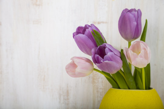 Bouquet of tulips in a yellow vase on a wooden background.