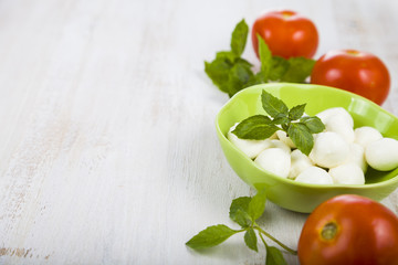 Mozzarella in a green plate on a wooden table. Mozzarella balls with basil leaves and tomato on a wooden board.