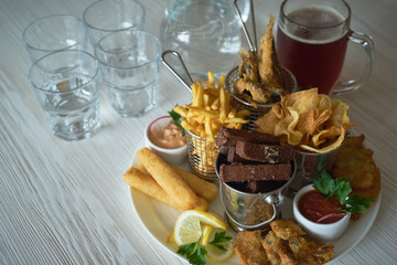 Food image: Plate of appetizers: rye garlic croutons with coarse sea salt, fish and chips, potato chips, cheese sticks, breaded and sauces on a light textural 