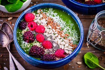 Green spinach smoothie bowl with raspberry,.blackberry,.flax seeds, sunflower seeds and coconut chips