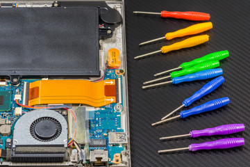 disassembled laptop motherboard on carbon background with rainbow collection of screwdrivers