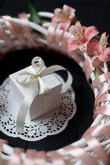 White gift box with white bow inside wreath with flowers on wooden black background