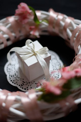 White gift box with white bow inside wreath with flowers on wooden black background