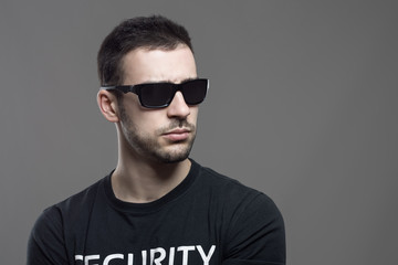 Obraz premium Macho tough security agent wearing sunglasses looking away at copyspace. Atmospheric contrasty portrait over gray studio background.