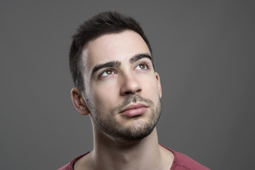 Fototapeta premium Close up of young handsome man face looking up thinking. Atmospheric contrasty portrait over gray studio background.