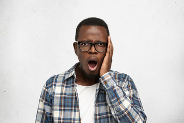 Strong human emotions, feelings and facial expressions. Attractive Afro-American man shocked and upset with radio news about petrol price rising, keeping mouth opened, isolated on white background