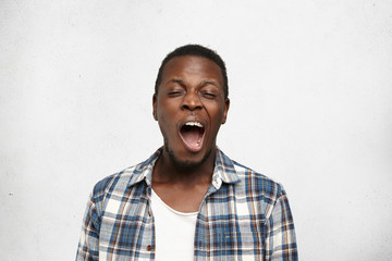 Headshot of young bored black man, yawning isolated on light background. Facial expressions, feelings, body language. College student after long hours of doing homework, chronic fatigue of exams - obrazy, fototapety, plakaty