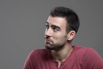 Moody portrait of disinterested sulking male face looking at copy space over gray studio background
