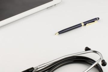 Tablet computer, metal gold-blue pen and stethoscope on a white background