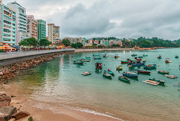 Fototapeta premium Hong Kong, China - January 30, 2016: Fishing boats rest in Stanley Bay by seashore on buildings background. Beautiful scenic landscape of Stanley waterfront in the evening