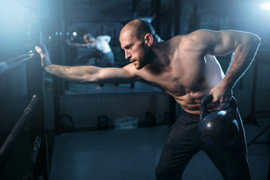 Muscular athlete workout, man lifting kettlebell
