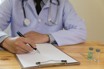 doctor writing RX prescription in medical office clinic with drugs on desk