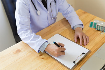 doctor writing RX prescription in medical office clinic with drugs on desk