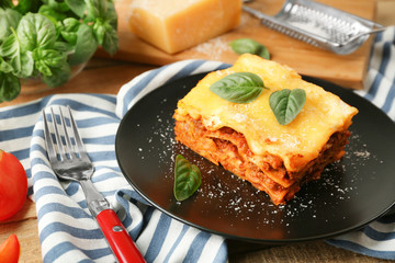 Black plate with delicious lasagna and striped napkin, closeup