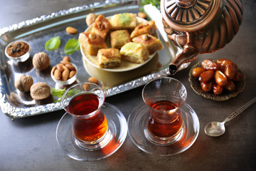Pouring Turkish tea into traditional glass and sweets on table closeup