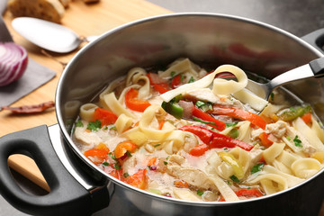 Spoon with chicken noodle soup over saucepan, closeup