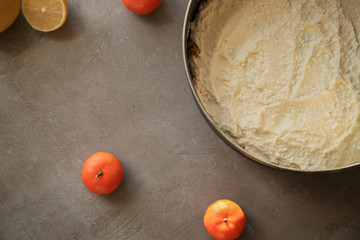 Cheesecake in baking form and citrus fruits on kitchen table