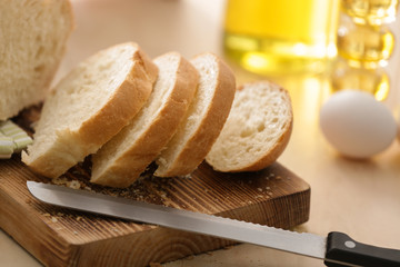 Wooden board with cut bread and knife on kitchen table