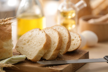 Wooden board with cut bread and knife on kitchen table