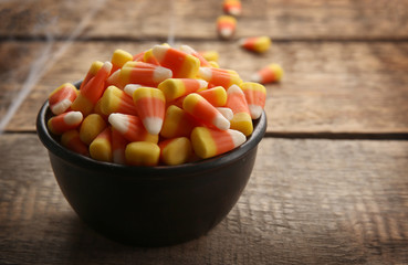 Bowl with tasty Halloween candies on wooden background