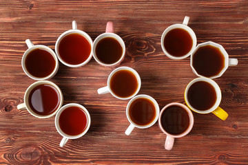Delicious tea in cups forming spiral on wooden background