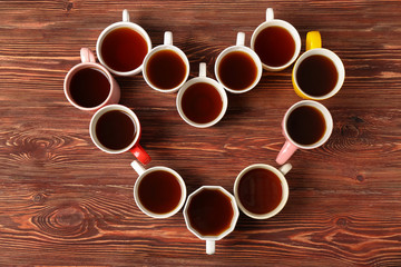 Obraz na płótnie Canvas Delicious tea in cups forming heart on wooden background